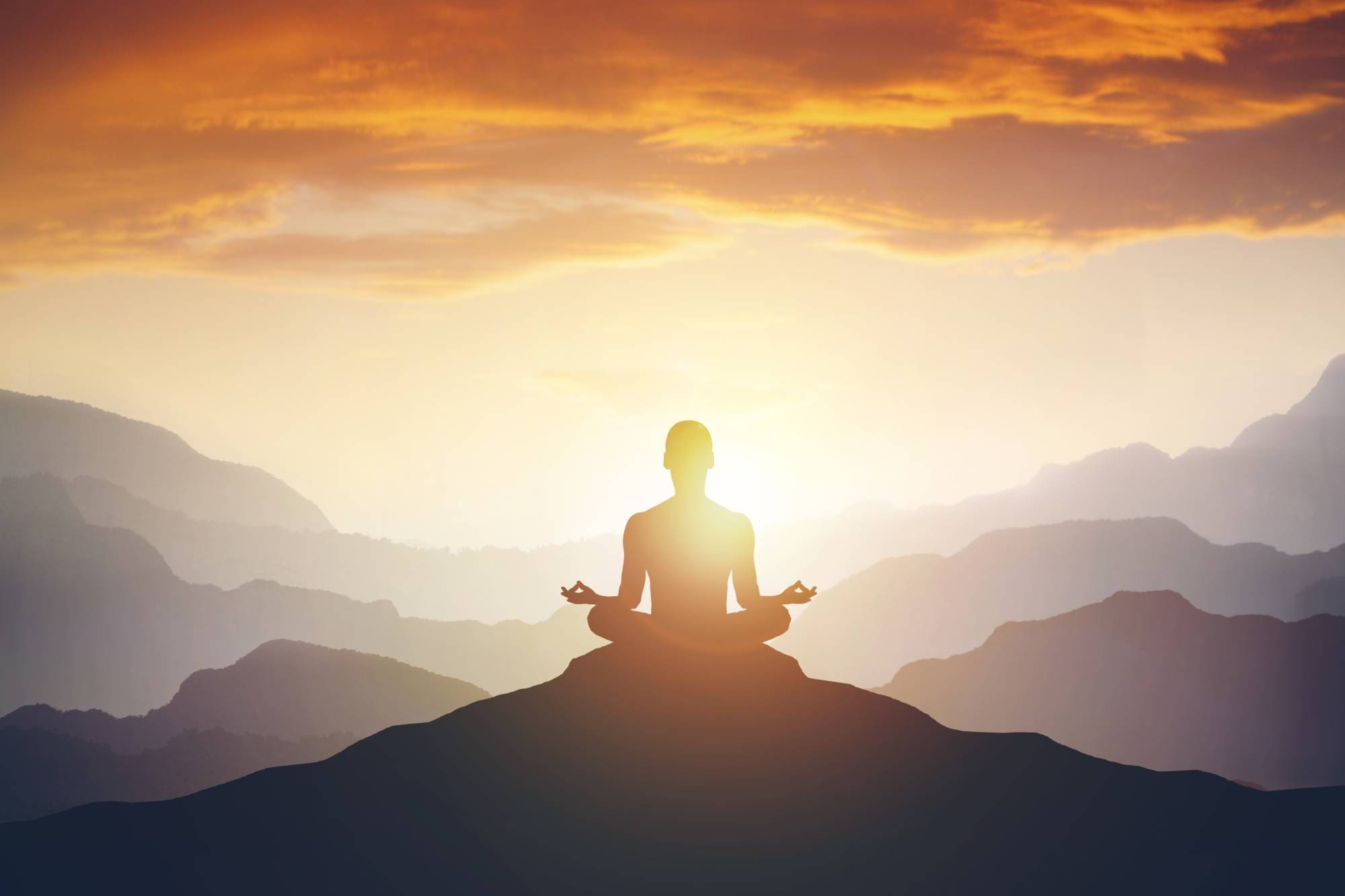 A person sitting in the middle of a mountain with sun shining.
