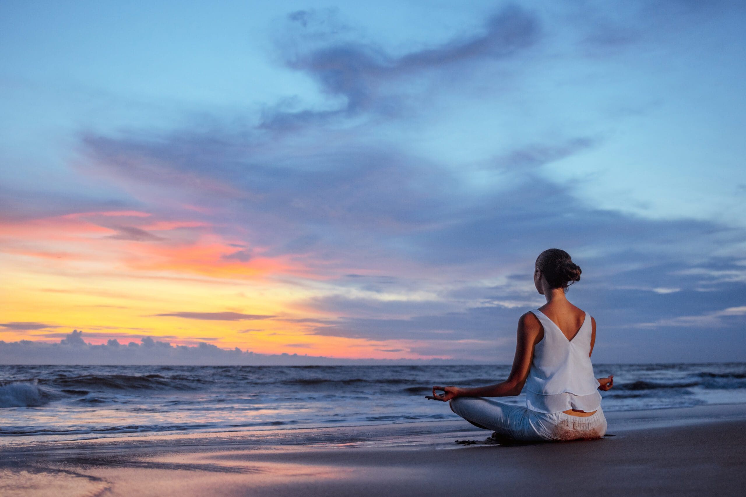 Person meditating on beach at sunset.
