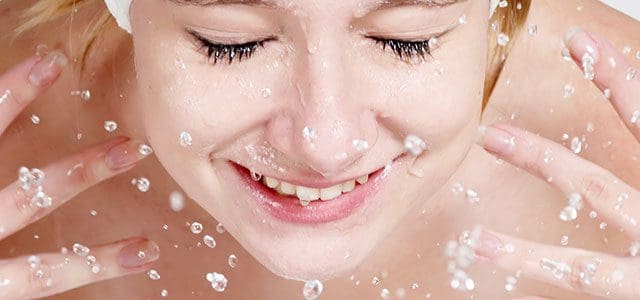 Smiling woman splashing water on face.